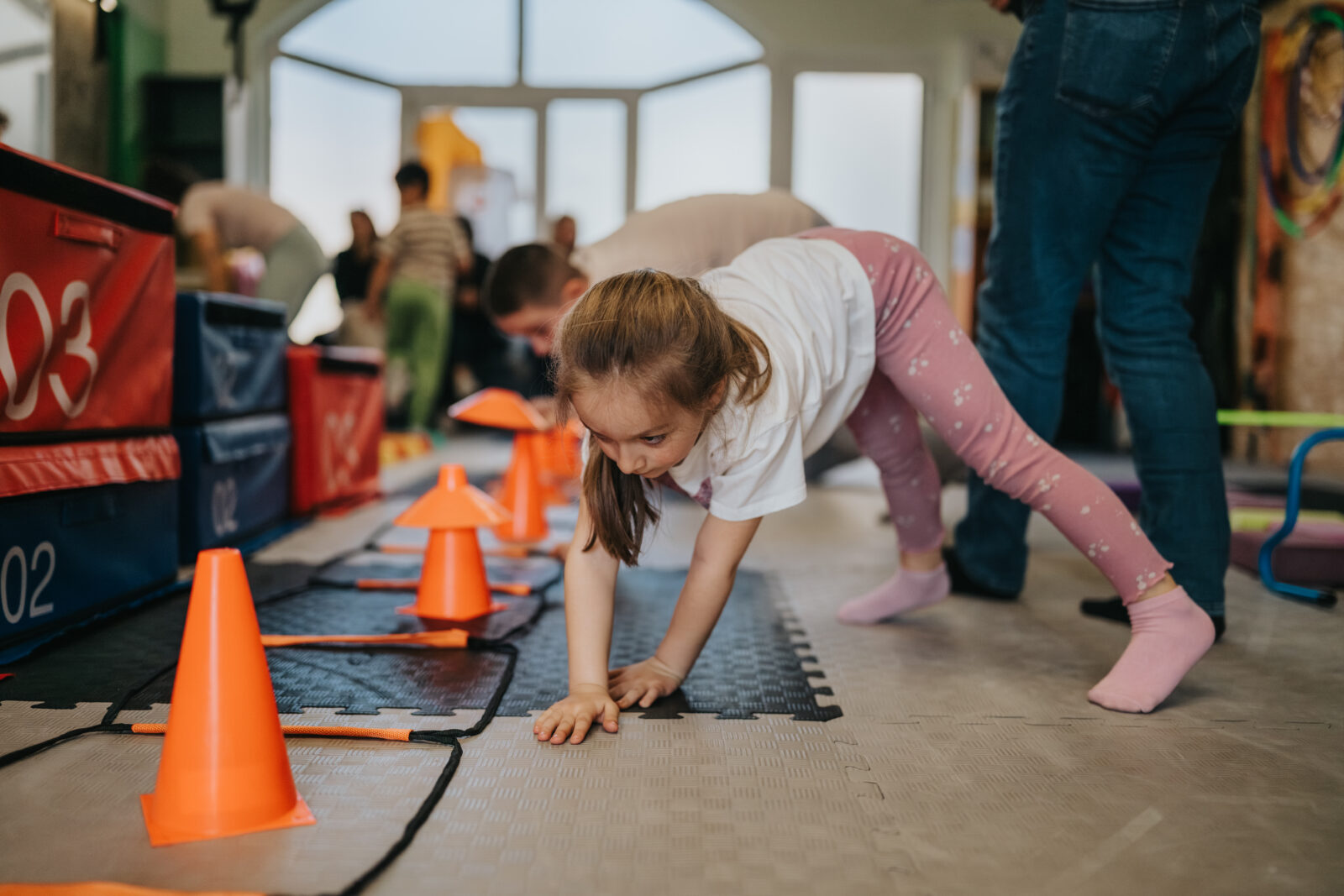 Kids fitness class girl crawling through indoor obstacle course during group exercise session